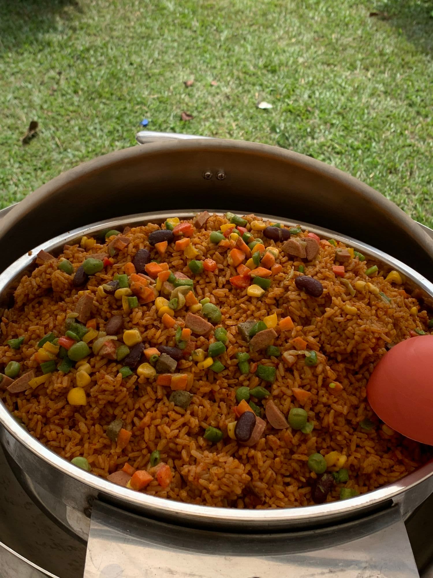 A serving dish of jollof rice with sweetcorn, peas and carrots