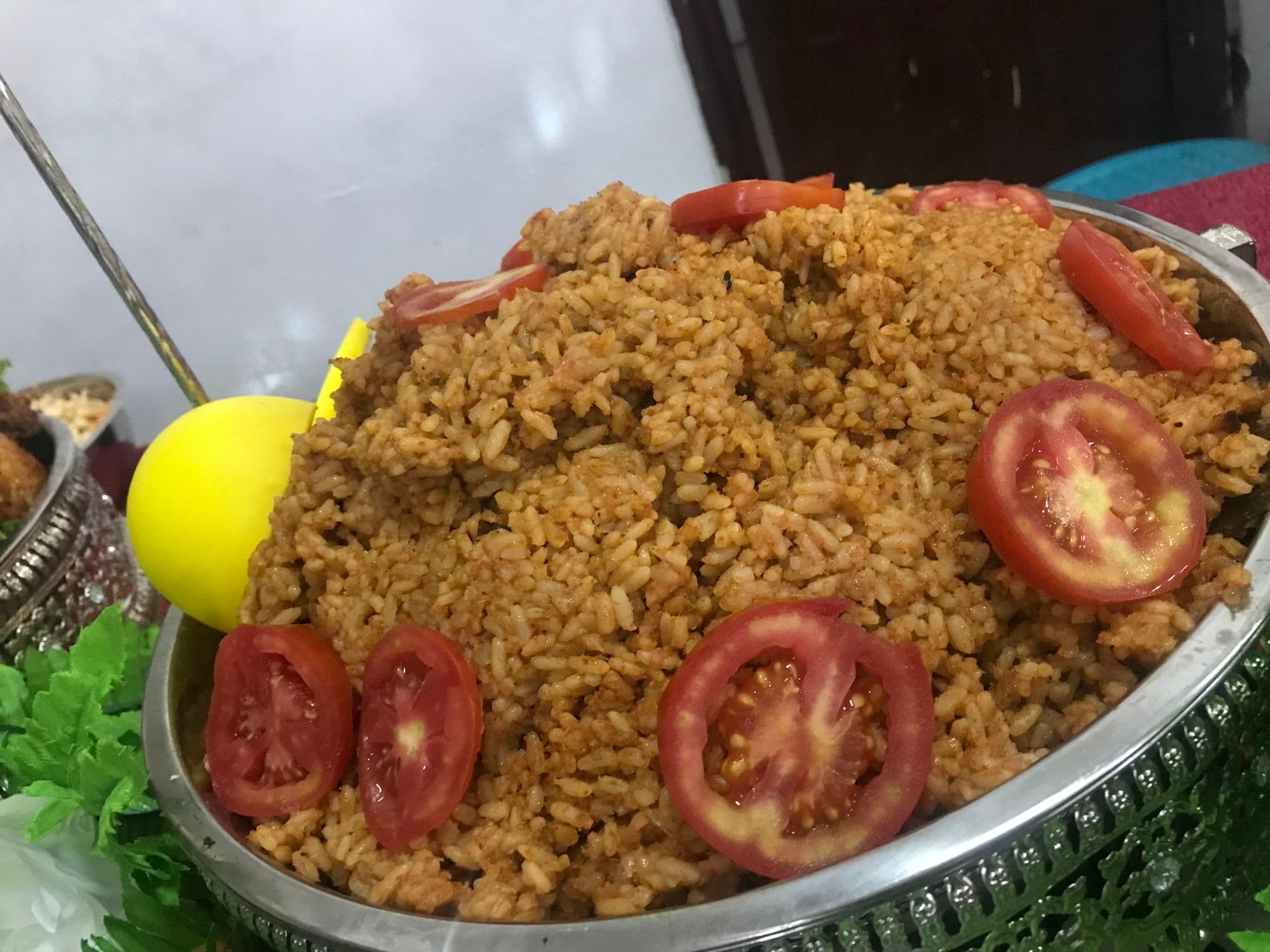 Jollof rice topped with fresh tomato slices on a silver platter