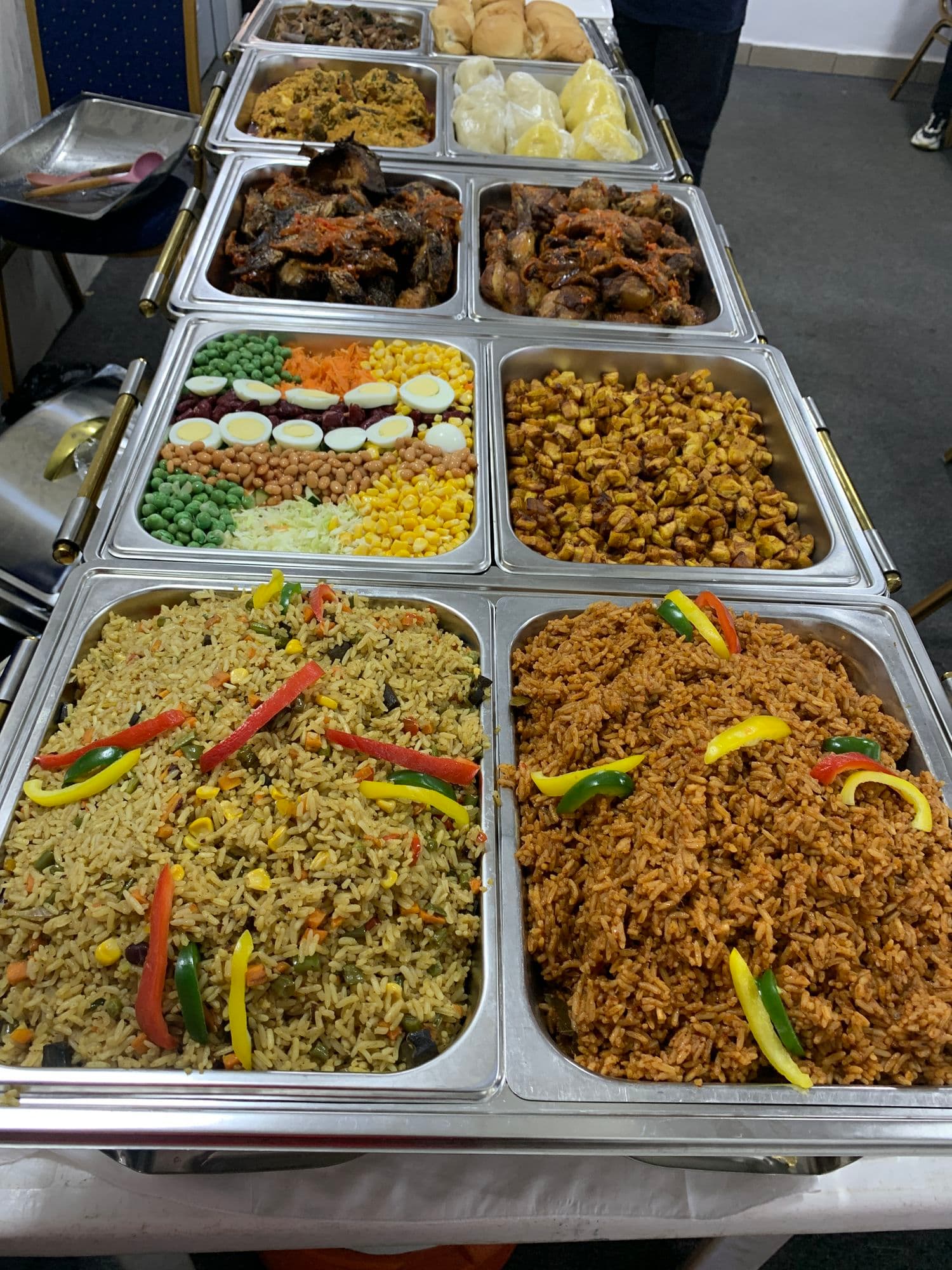 A buffet spread of jollof rice, fried rice, beef, plantain and salad