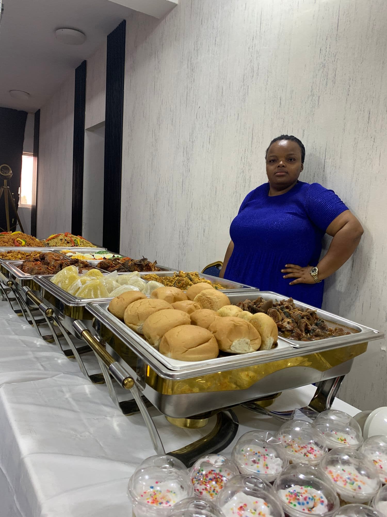 A host standing beside a buffet table of bread rolls, stews and grilled meat