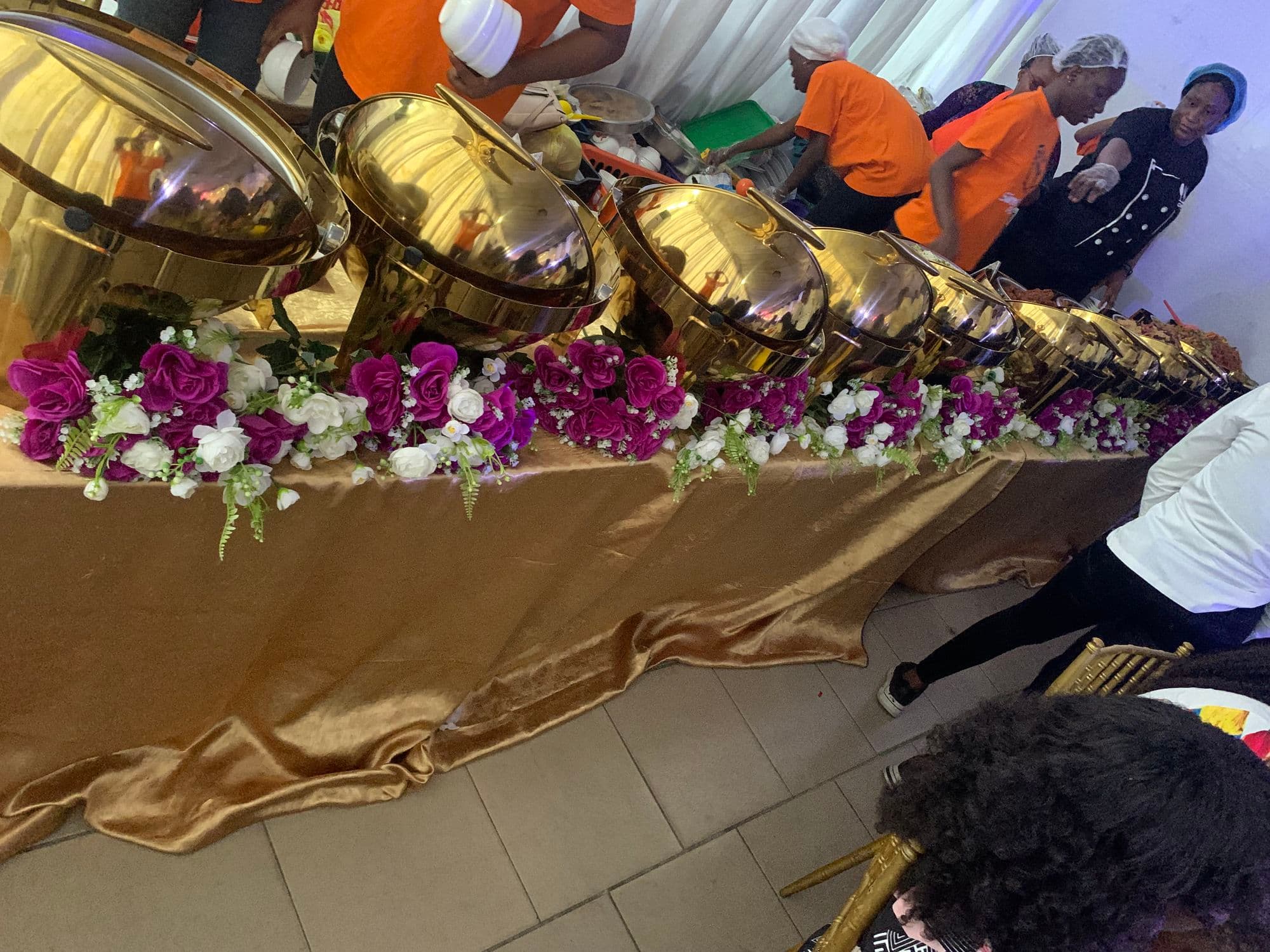A row of gold serving dishes on a buffet table decorated with flowers