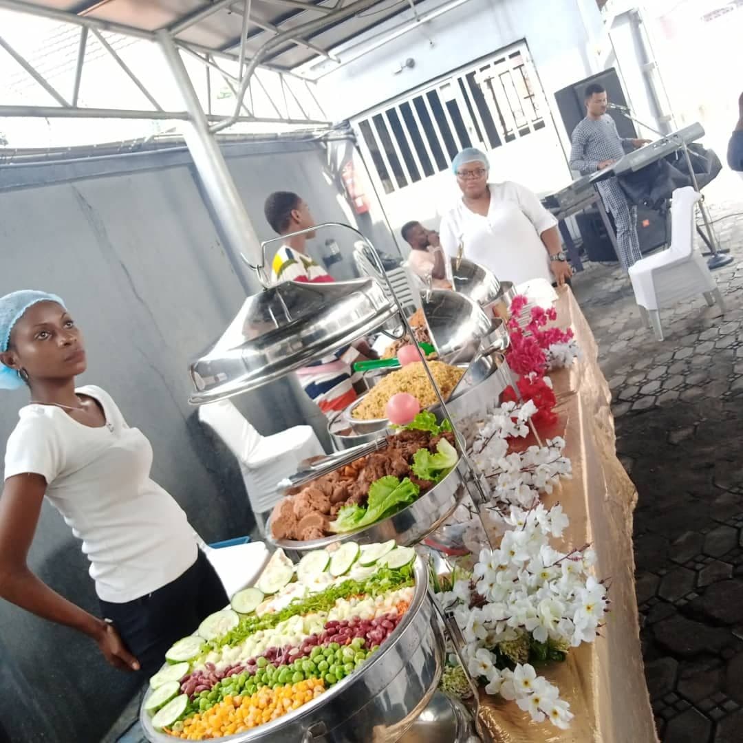 A cook standing beside an outdoor buffet line of covered dishes and salads