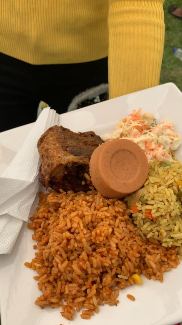 A plate of jollof rice, fried rice, grilled meat, moi moi and coleslaw
