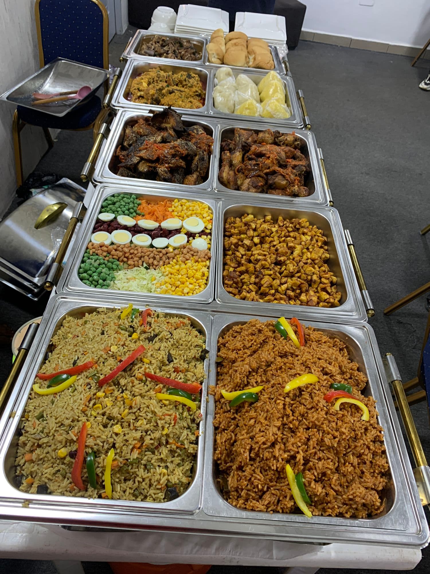 Trays of jollof rice, fried rice, beef and vegetables on a buffet